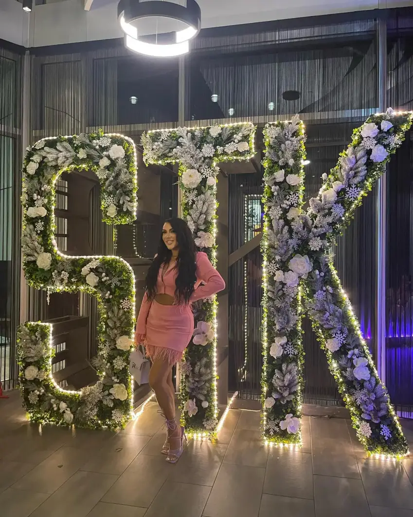 A woman stands confidently in front of a large sign displaying the letters "stk."